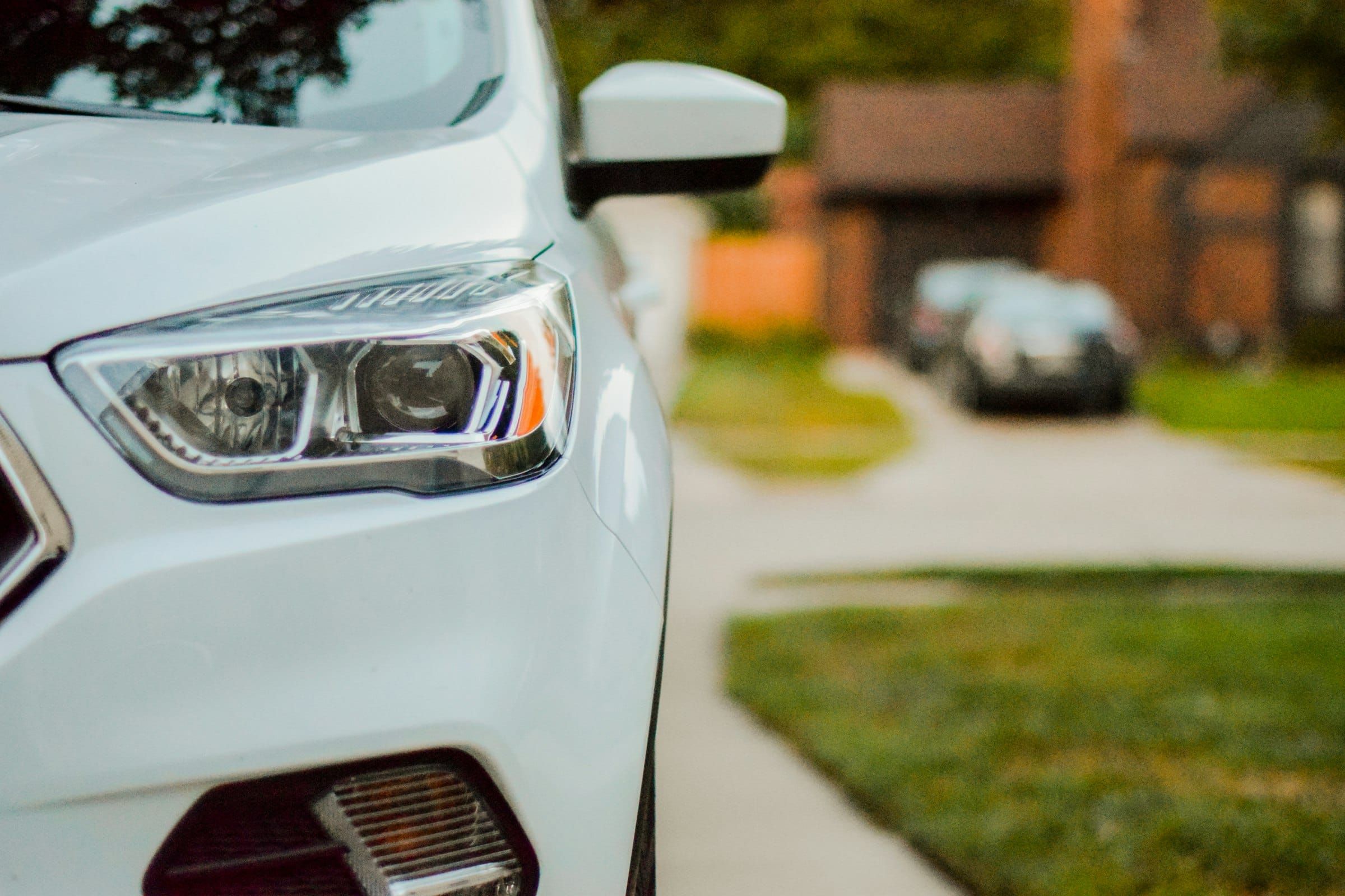 Close-up of the headlight and front wing of a white car parked on a suburban street