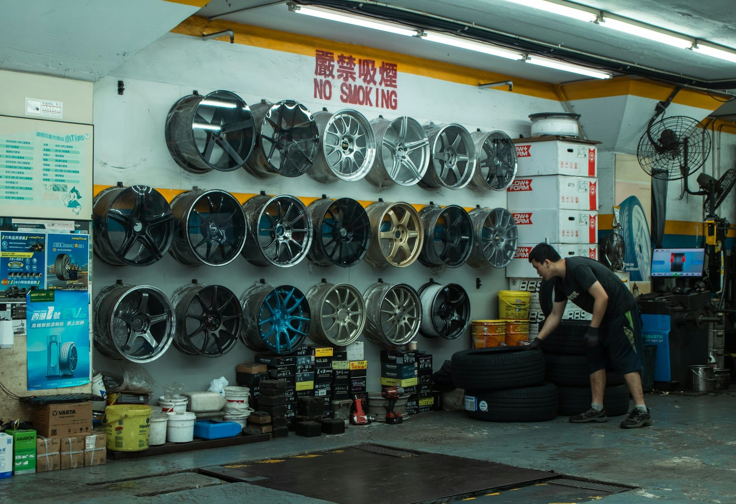 A mechanic stacking car tyres in a workshop with wheel rims mounted on the wall