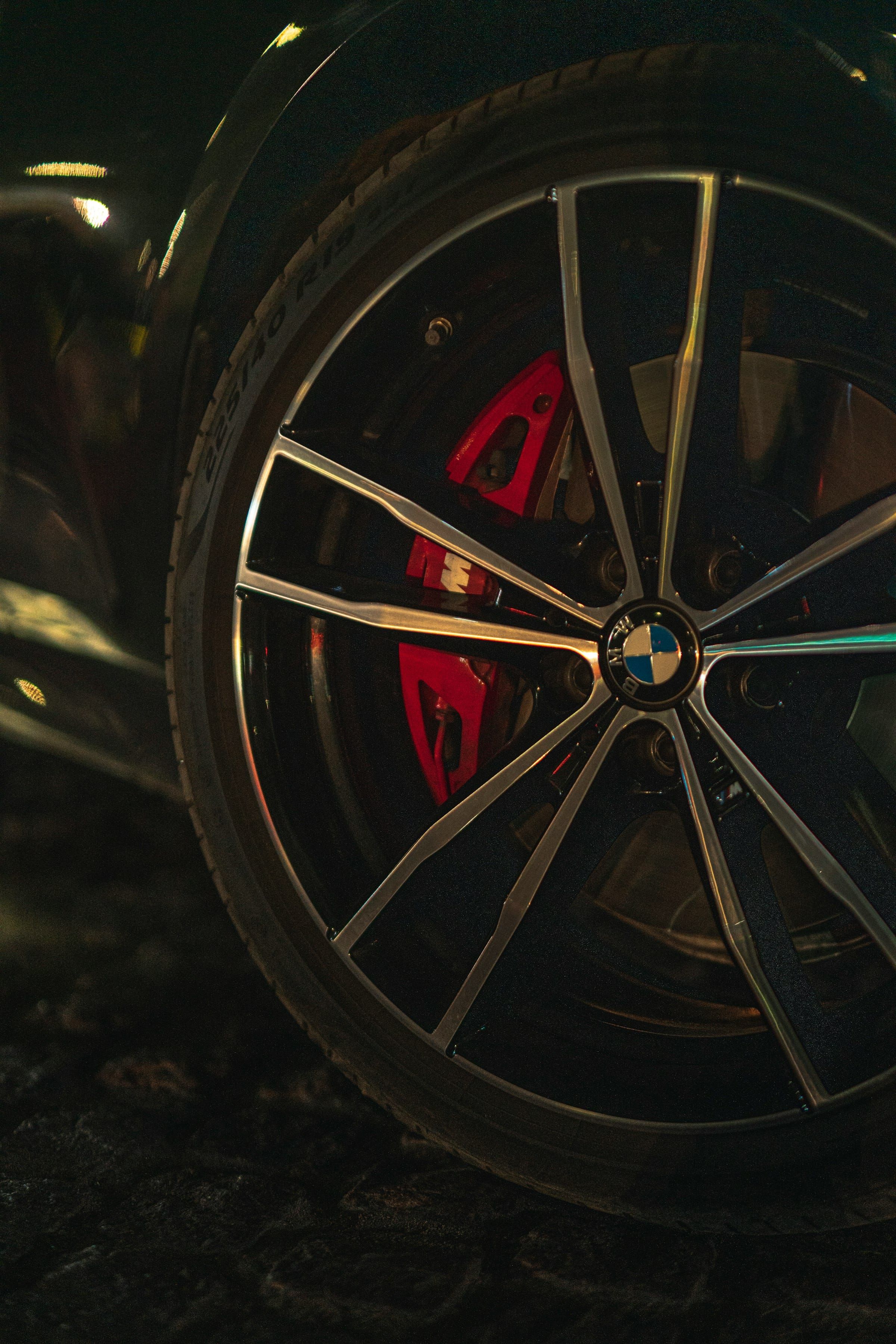 Close-up of a black multi-spoke alloy wheel with a red brake calliper, in low light